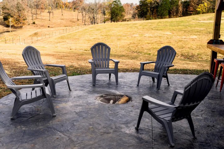 Five grey chairs on a patio surrounding a fire pit.